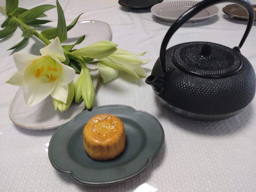 百合の花、緑色のお皿に置かれた月餅、黒い鉄瓶の写真